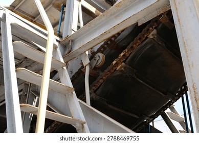 Rusty metal framework supports complex mechanical systems in a factory setting.