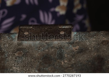 Rusty metal hinge fixed to a weathered stone surface inside a traditional village home in Birbhum West Bengal under dim indoor shadows reflecting systemic poverty and the slow passage of time for aging and hardship concepts.