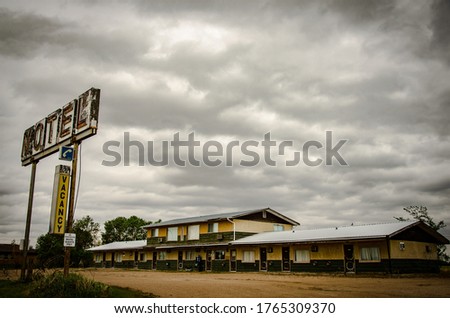 A rusty metal motel sign with wooden old motels under the cloudy and rainy  sky