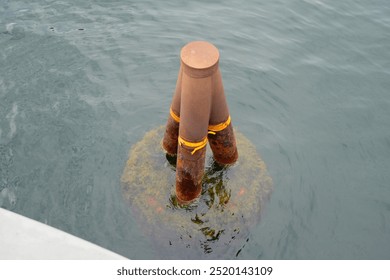 Rusty metal object submerged in greenish water near a wooden pier, with algae visible around the base and reflective ripples on the water’s surface. The scene captures a serene waterfront environment - Powered by Shutterstock