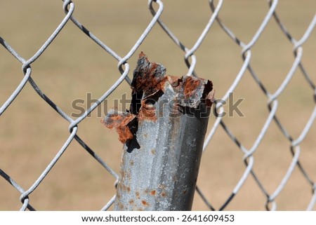 Rusty metal post in front of a chain link fence