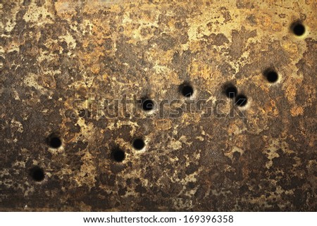 Rusty metallic surfaces perforated with bullet holes.
