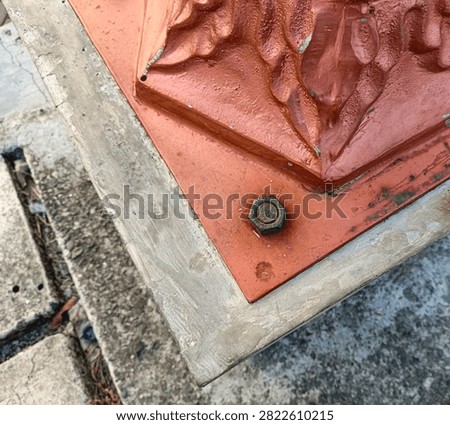 Rusty rusty nut and bolt securing a painted metal base on a concrete structure, close-up view.