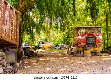 Rusty old abandoned red truck/ trailer head in junk yard/ junkyard/ scrapyard and other discarded salvage cars/ vehicles around.  Outdoor countryside park with automobile wreckage metal parts debris. - Shutterstock ID 1589443210