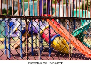 Rusty Old Chain Link Fence With Colorful Playground Equipment In Background.