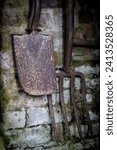 Rusty old gardening tools shovel and fork hanging on mossy brick wall