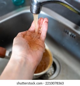 Rusty Orange Water Flows From The Kitchen Faucet Onto A Man's Hand
