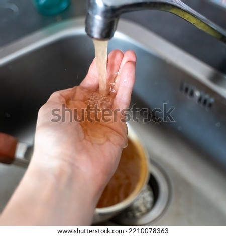Rusty orange water flows from the kitchen faucet onto a man's hand