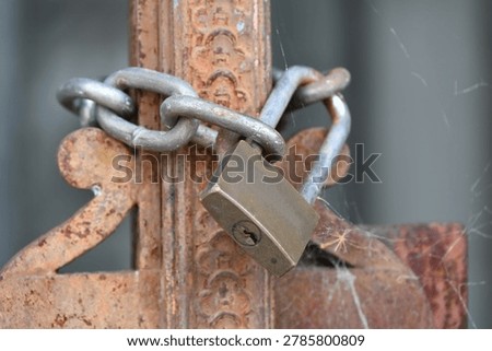 Rusty padlock securing an old metal gate with a chain and latch mechanism.