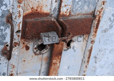 Rusty padlock securing an old metal gate with a chain and latch mechanism.