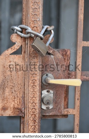 Rusty padlock securing an old metal gate with a chain and latch mechanism.