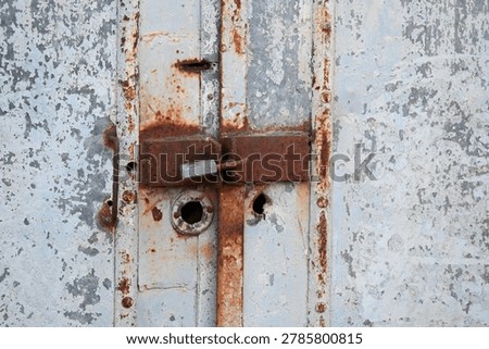 Rusty padlock securing an old metal gate with a chain and latch mechanism.
