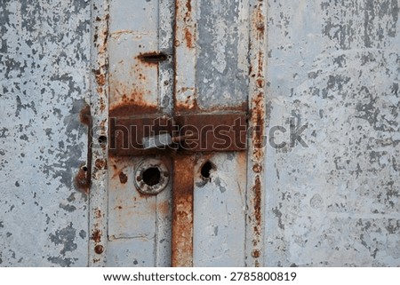 Rusty padlock securing an old metal gate with a chain and latch mechanism.
