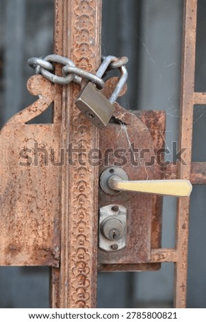 Rusty padlock securing an old metal gate with a chain and latch mechanism.