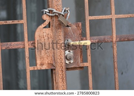 Rusty padlock securing an old metal gate with a chain and latch mechanism.