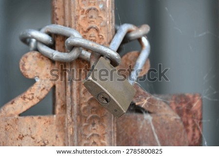 Rusty padlock securing an old metal gate with a chain and latch mechanism.