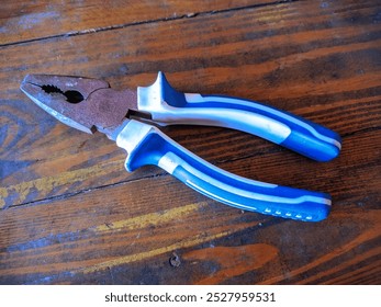 A rusty pair of pliers with blue and white handles on a wood grain background - Powered by Shutterstock