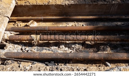 A rusty pipe is laying on the ground. The pipe is old and has a lot of rust on it. The ground is dirty and has some debris on it