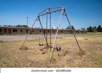 Rusty playground equipment with a swingset sits in a courtyard of an abandoned motel