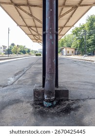 A rusty rain gutter on a column under the afternoon roof of a train station platform. Perfect for urban travel and infrastructure themes with tracks and shelter.