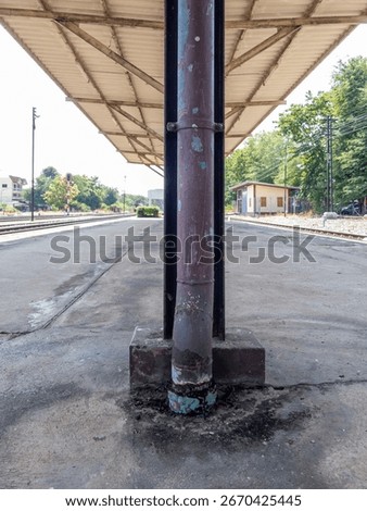 A rusty rain gutter on a column under the afternoon roof of a train station platform. Perfect for urban travel and infrastructure themes with tracks and shelter.