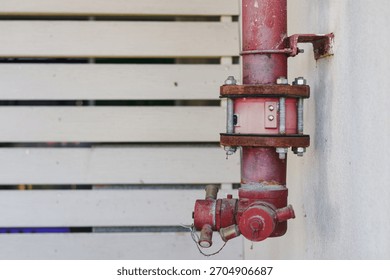 A rusty red fire hydrant valve mounted on a wall.