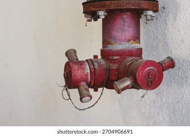 A rusty red fire hydrant valve mounted on a wall.