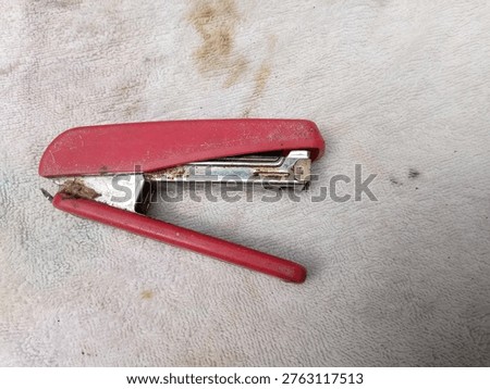 Rusty red stapler tool on textured fabric for office equipment concept and product photography JPG