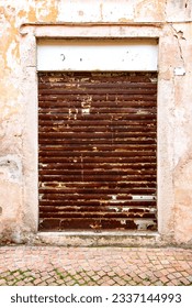 Rusty roller shutter of an ancient shop in old town of Luino, Italy. Rotten corroded metal door gate in a lost place with filthy white facade. Closed door in ruined entrance of bankrupt business.