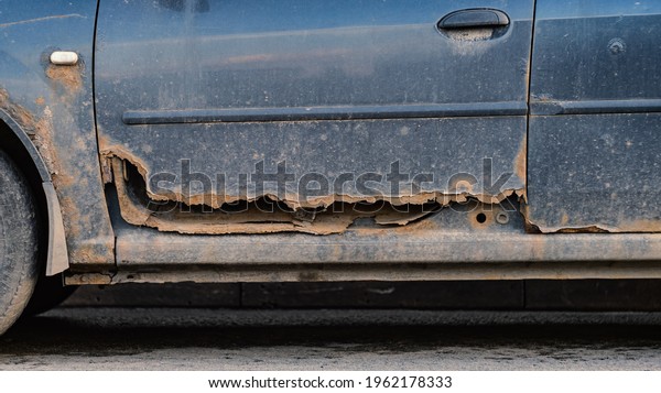 Rusty rotten car driver\'s door close up view.\
Deicing agents and high humidity. Corrosion resistance, galvanizing\
of the car body.