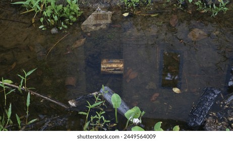 Rusty tin can in a muddy puddle. This photo shows a rusty tin can floating in a muddy puddle. The can is partially submerged in the water, and its surface is covered in dirt, leaves, and other debris.