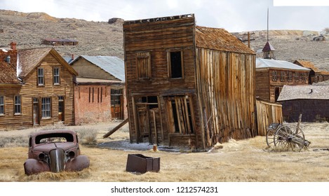 Rusty vintage car and idyllic wooden houses decay in the American wilderness after the gold rush. Scenic view of a ghost town in the Californian countryside slowly falling apart in rugged conditions.