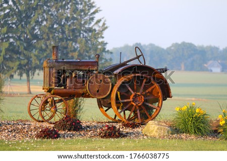 a rusty vintage farm tractor on display in a rural farm with bright flowers early morning