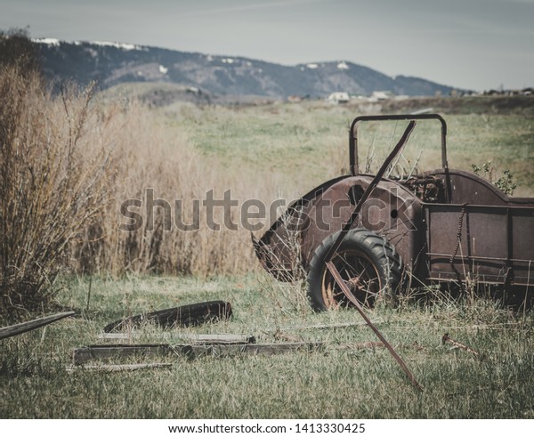 Rusty vintage hay baler\
cart sitting abandoned in a farm field in Spring surrounded by\
scraps of wood.