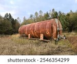 A rusty water or liquid tank abandoned in the middle of the forest. The problem of ecology