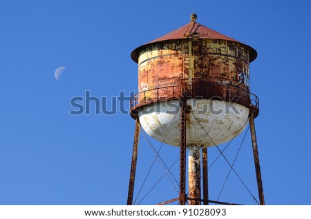Rusty water tower in a cloudless sky with crescent moon