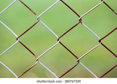 Rusty Wire Grid On Green Background. Galvanized Iron Chain Link Fencing Mesh Backdrop. Rusty Chain-link Fence With Green Blurred Background, Closeup. Old Chain-wire Fence, Cyclone Fence, Woven Fence.