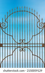 Rusty wrought iron gate with sharp points against a blurred clear blue sky with clouds and copy space. Brescia, Lombardy, Italy, Europe.