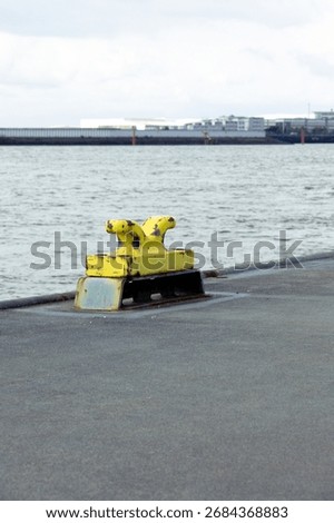 Rusty yellow dockside bollard fixed on harbor quay beside water under cloudy sky