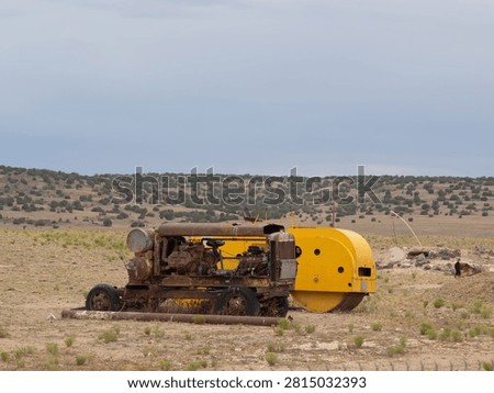 Rusty yellow old air compressor, likely used for industrial or mining purposes, rests in arid field. Dusty terrain stretches under cloudy sky