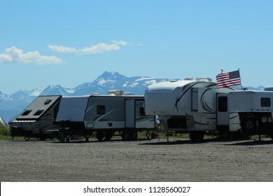 RV Campers Lined Up On Homer Spit, Alaska With American Flag Flying Overhead And Mountains Behind