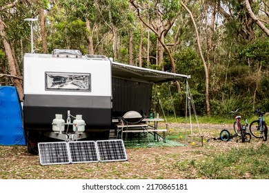 RV caravan camper on a campsite in the bush forest nature. Awning, portable toilet, solar panels, bbq, table. Family camping set up - Shutterstock ID 2170865181