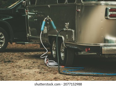RV Park Full Hookups. Travel Trailer Connected to Water and Power. Camping Hose Filter Attached. Recreational Vehicles and Campground Theme. - Shutterstock ID 2077152988