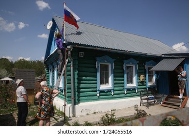 Ryazan Oblast, Russia. 9 May 2019. A Man In A Cap And With A St. George Ribbon Sets The Russian Flag On The Roof Of His Traditional Russian Wooden House In Honor Of The Russian Holiday Victory Day.