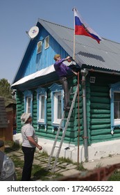 Ryazan Oblast, Russia. 9 May 2019. A Man In A Cap And With A St. George Ribbon Sets The Russian Flag On The Roof Of His Traditional Russian Wooden House In Honor Of The Russian Holiday Victory Day.