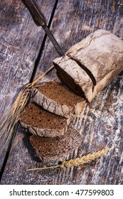 Rye bread, dark, fragrant, cut into thin slices with a knife on a wooden background