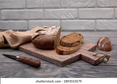 Rye bread round loaf cut into pieces on a wooden board with a knife made of rustic wood.