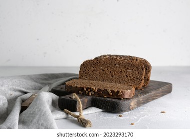Rye bread with seeds lies on a dark wooden board. A knife with a wooden handle on a light napkin
