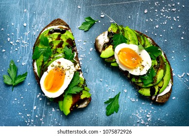 Rye toasts with soft cheese, avocado and boiled egg on a blue slate, stone or concrete background.Top view. - Powered by Shutterstock