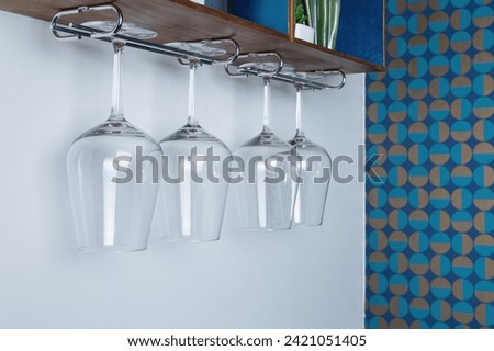 rystal wine glasses hang from a wooden rack. patterned retro wallpaper on the wall
